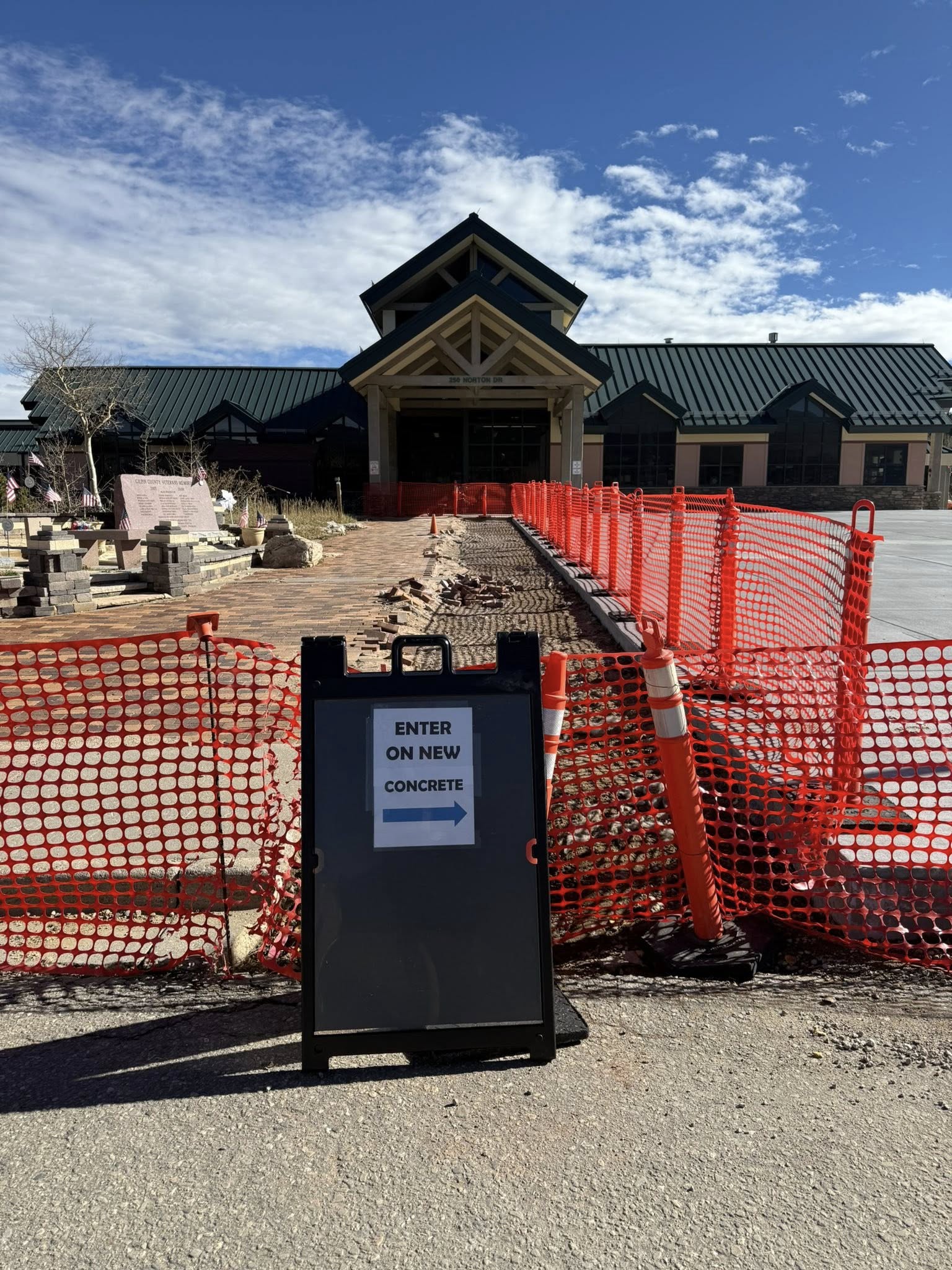 Entrance to the Community center displaying construction fencing and a sign indicating to enter on new concrete